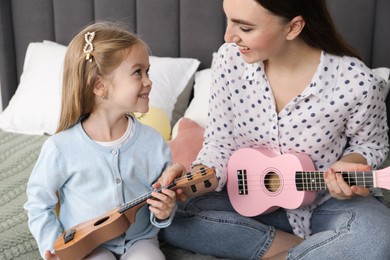 Photo of Young woman teaching little girl to play ukulele at home