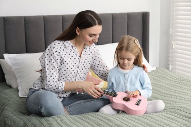 Photo of Young woman teaching little girl to play ukulele at home