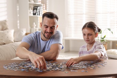 Photo of Happy father and his daughter solving puzzle together at wooden table indoors