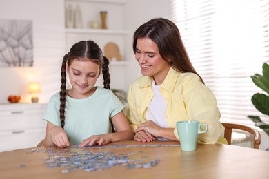 Photo of Happy mother and her daughter solving puzzle together at wooden table indoors