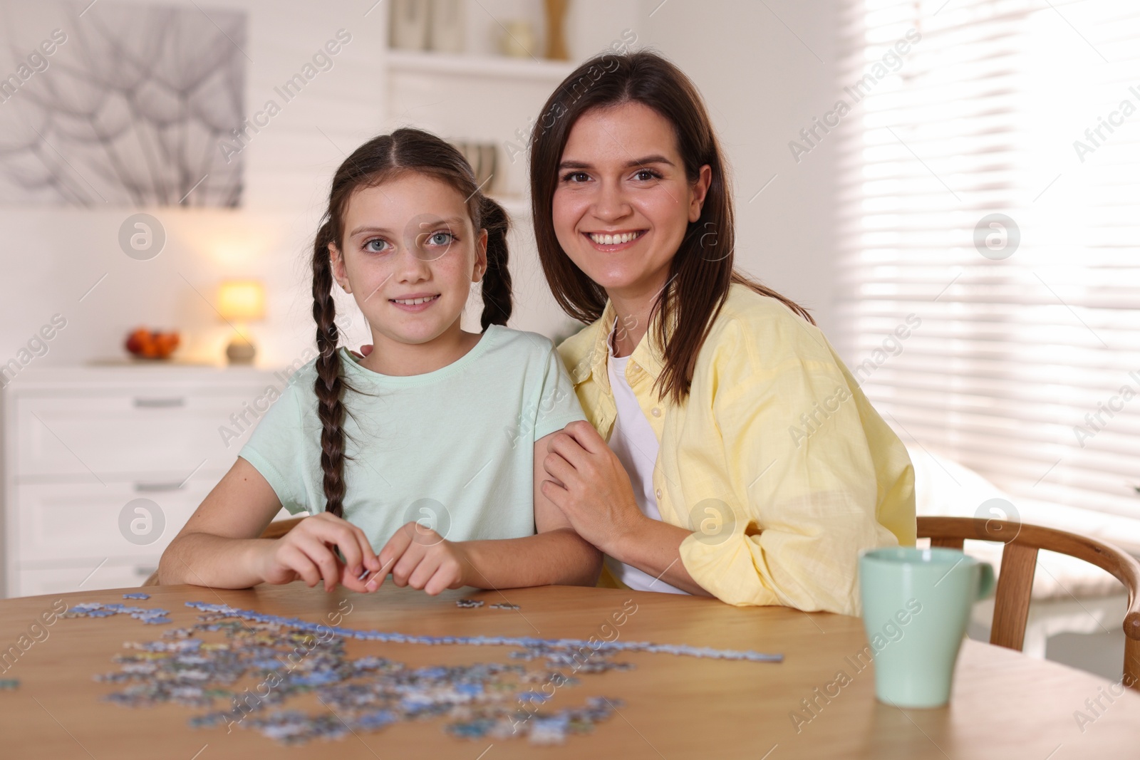 Photo of Happy mother and her daughter solving puzzle together at wooden table indoors