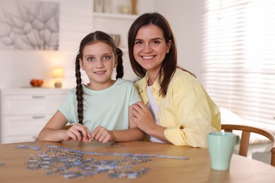 Photo of Happy mother and her daughter solving puzzle together at wooden table indoors