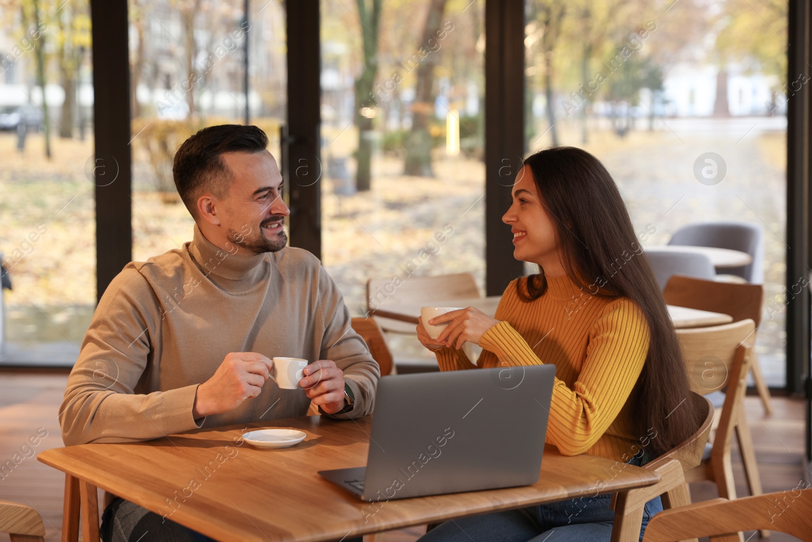 Photo of Colleagues with cups of coffee and laptop working together at table in cafe