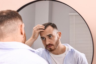 Photo of Baldness problem. Man with receding hairline near mirror in bathroom