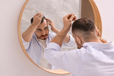 Photo of Baldness problem. Man applying serum onto hairline near mirror in bathroom