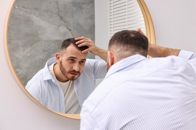 Photo of Baldness problem. Man with receding hairline near mirror in bathroom