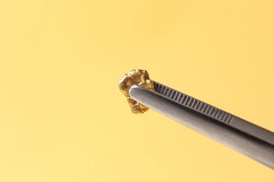 Photo of Tweezers with gold nugget against yellow background, closeup. Space for text