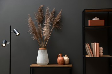 Photo of Console table with decor, lamp and shelving unit near grey wall in room. Interior design