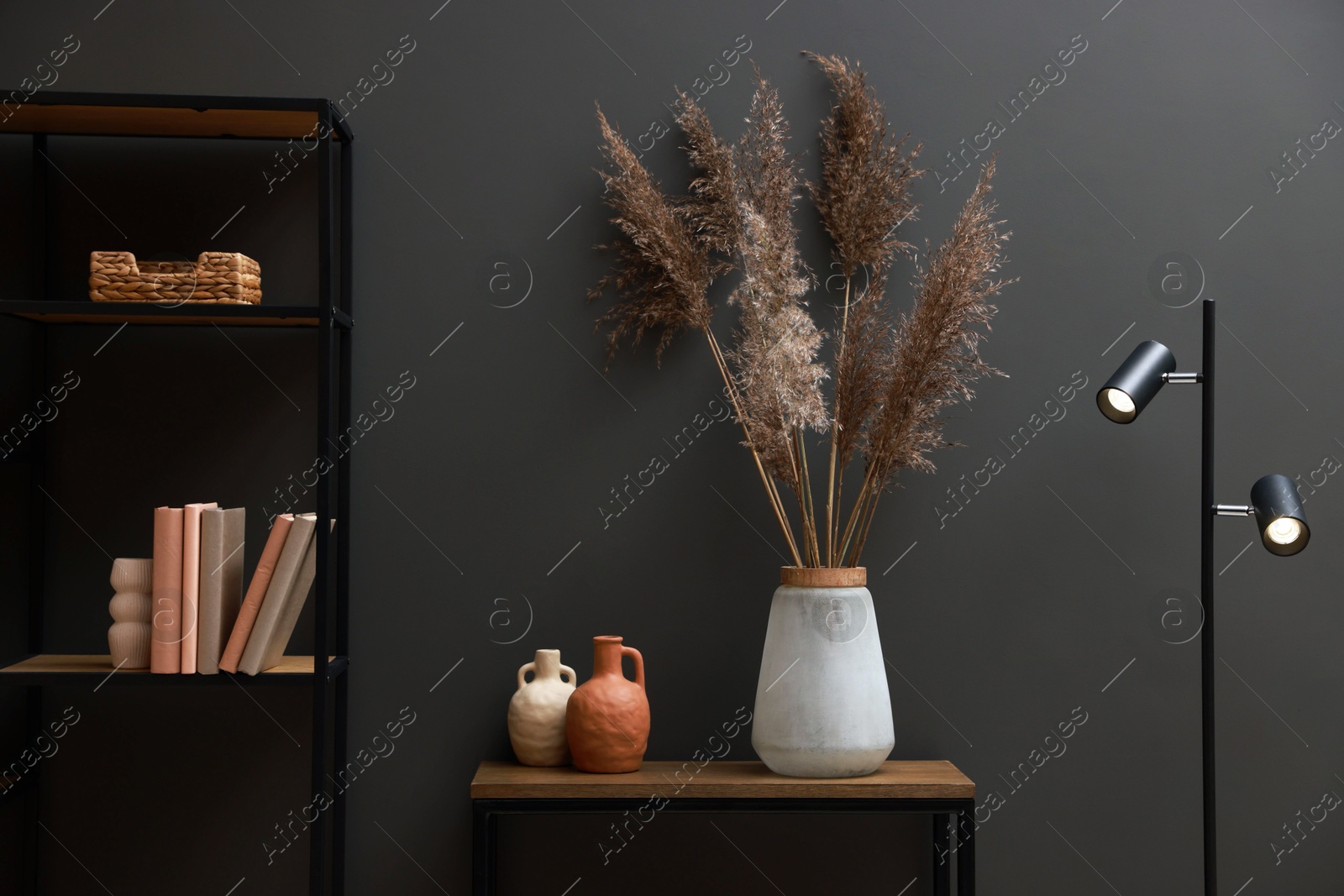 Photo of Console table with decor, lamp and shelving unit near grey wall in room. Interior design