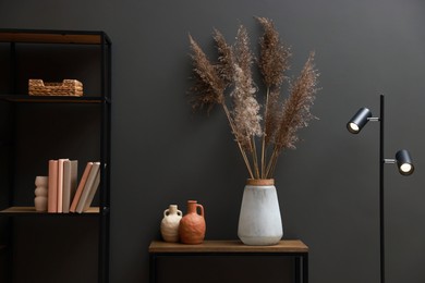 Photo of Console table with decor, lamp and shelving unit near grey wall in room. Interior design