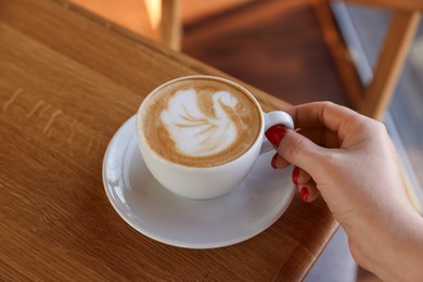 Photo of Woman with cup of aromatic coffee at wooden table in cafe, closeup