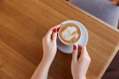 Photo of Woman with cup of aromatic coffee at wooden table in cafe, above view