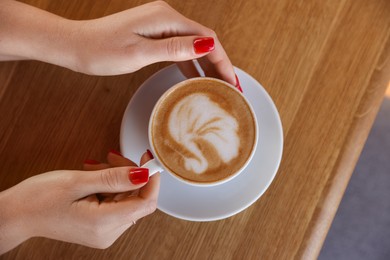 Photo of Woman with cup of aromatic coffee at wooden table in cafe, top view