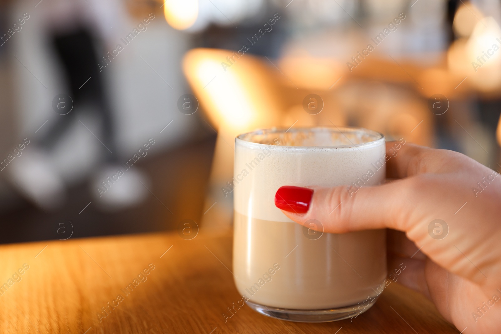 Photo of Woman with glass of aromatic coffee at wooden table in cafe, closeup. Space for text