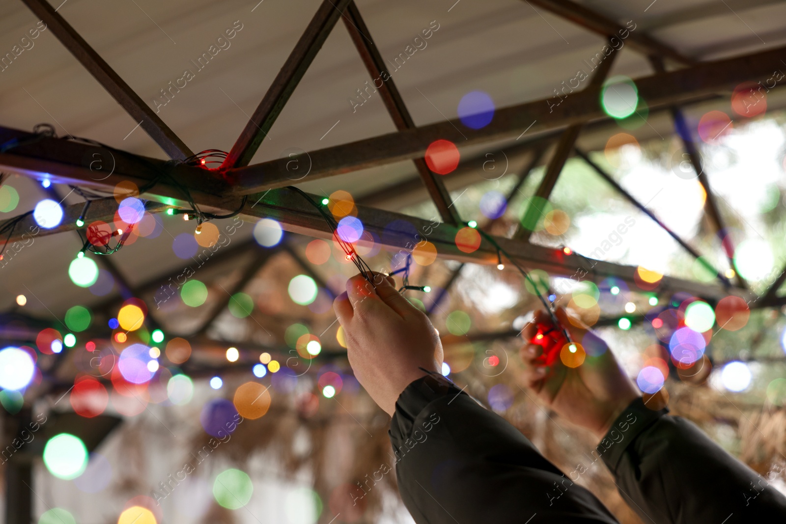 Photo of Man decorating house with Christmas lights outdoors, closeup