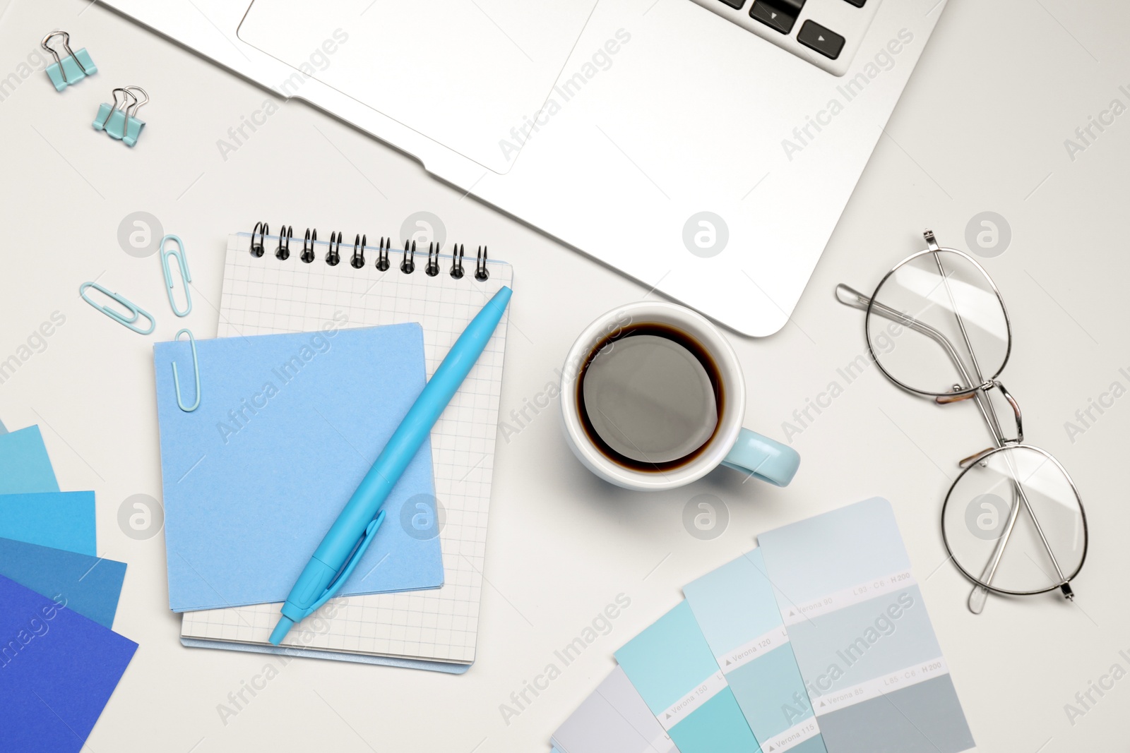 Photo of Designer's workplace with stationery, color palettes, cup of coffee and laptop on grey table, flat lay