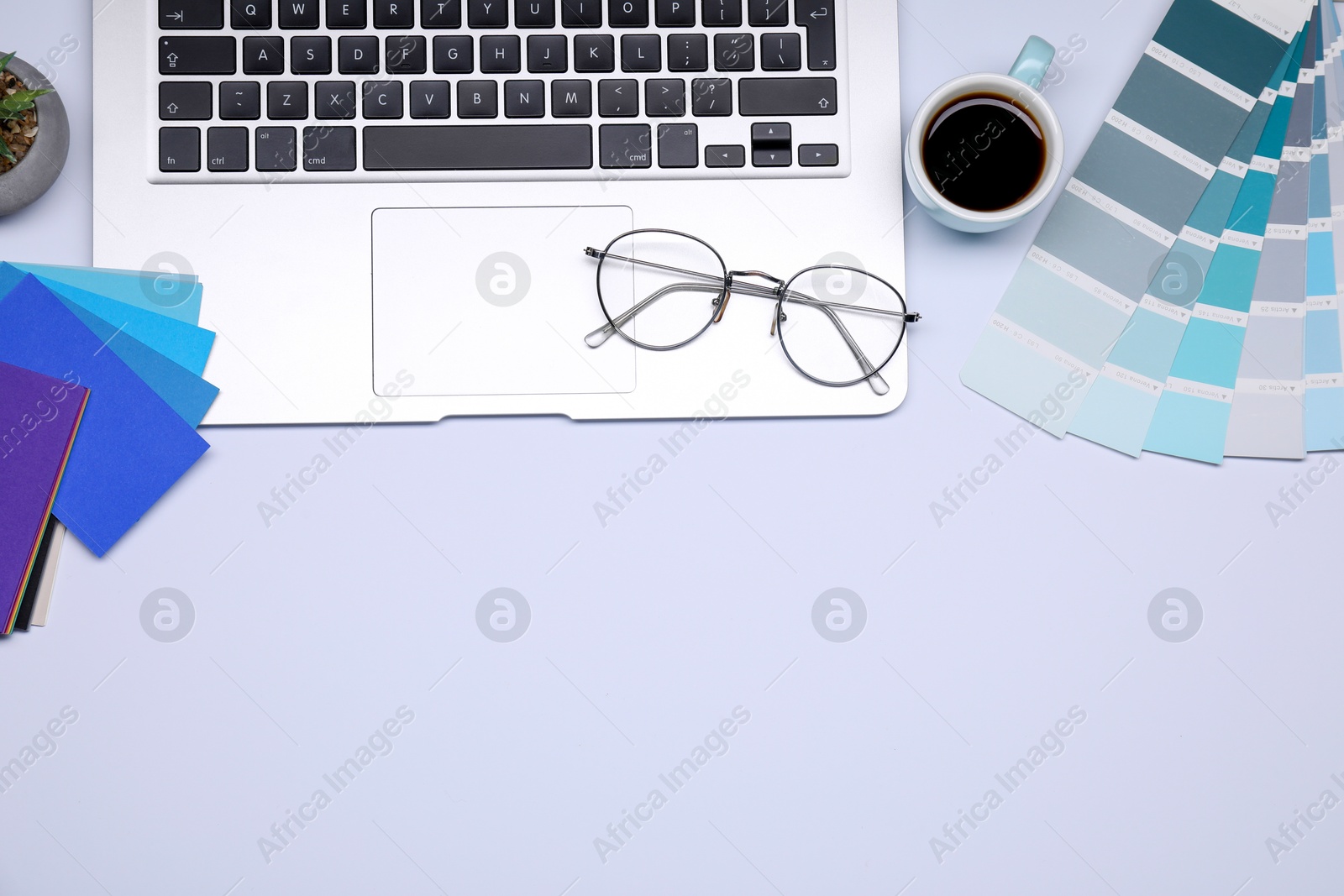 Photo of Designer's workplace with color palettes, cup of coffee, glasses and laptop on grey table, flat lay. Space for text