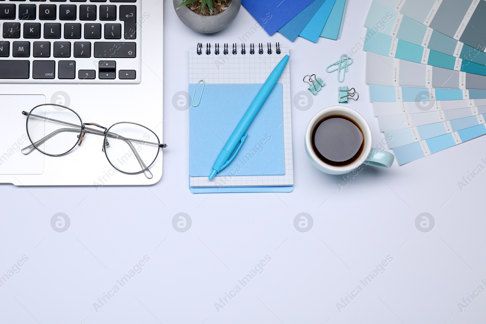 Photo of Designer's workplace with stationery, color palettes, cup of coffee and laptop on grey table, flat lay. Space for text