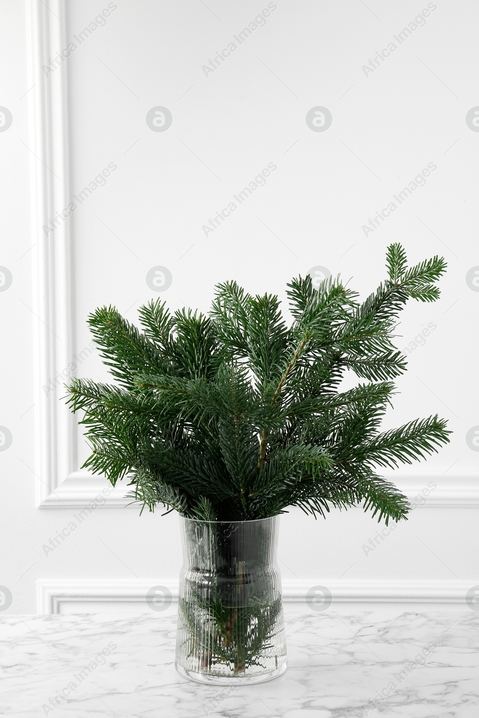 Photo of Beautiful fir tree branches on table near white wall. Christmas decor