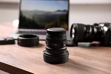 Photo of Professional photo camera, lens and laptop on wooden desk, selective focus