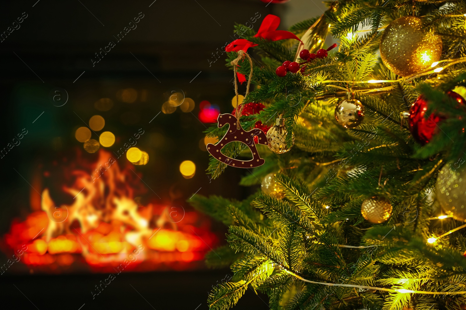 Photo of Beautiful Christmas tree decorated with horse toy, other ornaments and festive lights near fireplace at home, closeup. Bokeh effect