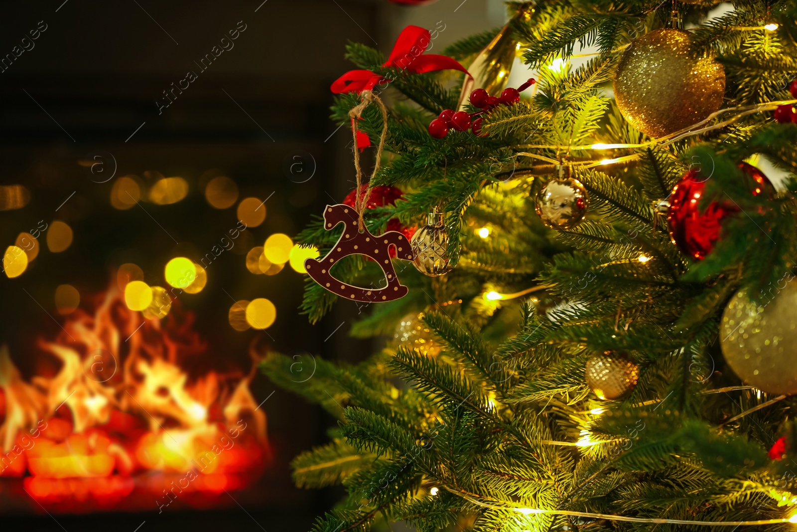 Photo of Beautiful Christmas tree decorated with horse toy, other ornaments and festive lights near fireplace at home, closeup. Bokeh effect