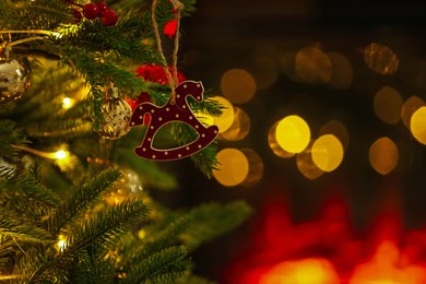 Photo of Beautiful Christmas tree decorated with horse toy, other ornaments and festive lights indoors, closeup. Bokeh effect