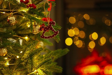 Photo of Beautiful Christmas tree decorated with horse toy, other ornaments and festive lights indoors, closeup. Bokeh effect