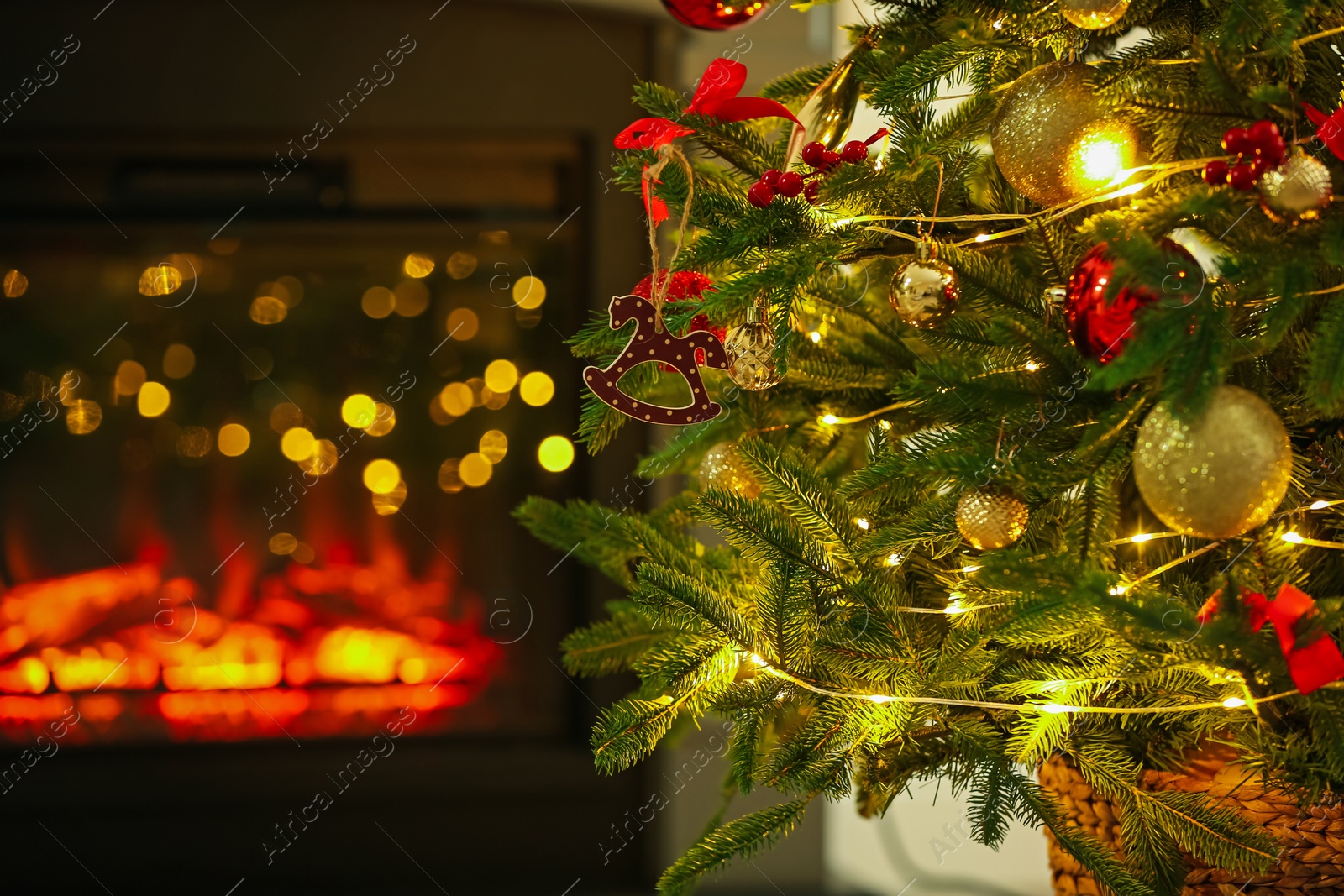 Photo of Beautiful Christmas tree decorated with horse toy, other ornaments and festive lights near fireplace at home, closeup. Bokeh effect