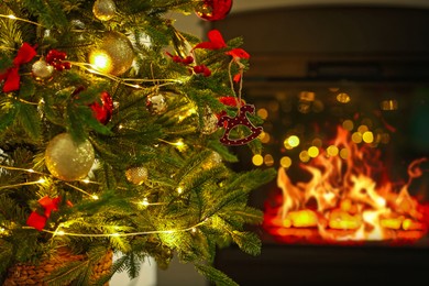 Photo of Beautiful Christmas tree decorated with horse toy, other ornaments and festive lights near fireplace at home, closeup. Bokeh effect