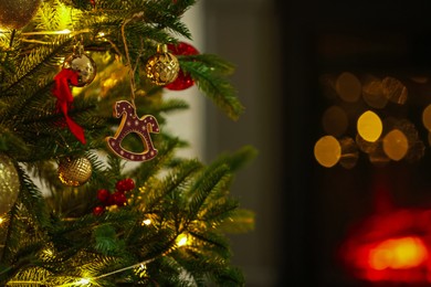 Photo of Beautiful Christmas tree decorated with horse toy, other ornaments and festive lights indoors, closeup. Bokeh effect