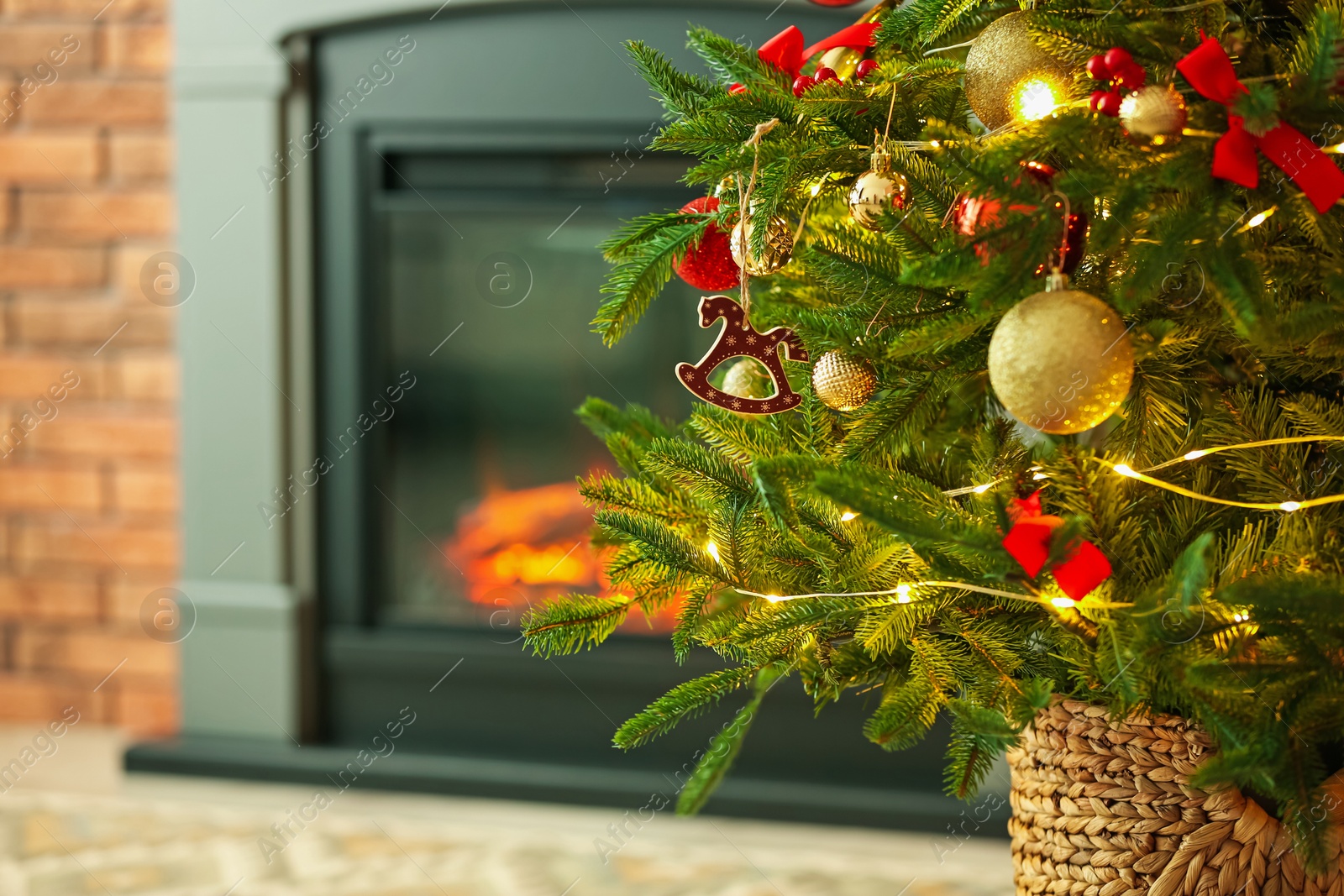 Photo of Beautiful Christmas tree decorated with horse toy, other ornaments and festive lights near fireplace at home, closeup. Space for text