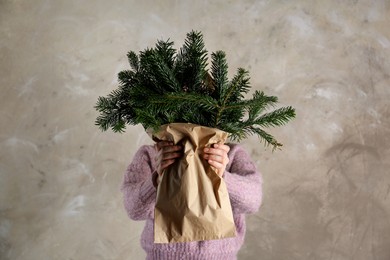 Photo of Woman holding green fir branches in paper bag near gray wall. Christmas decor