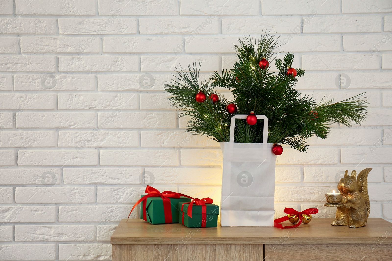 Photo of Beautiful Christmas composition of decorated fir and pine tree branches on wooden nightstand near white brick wall, space for text