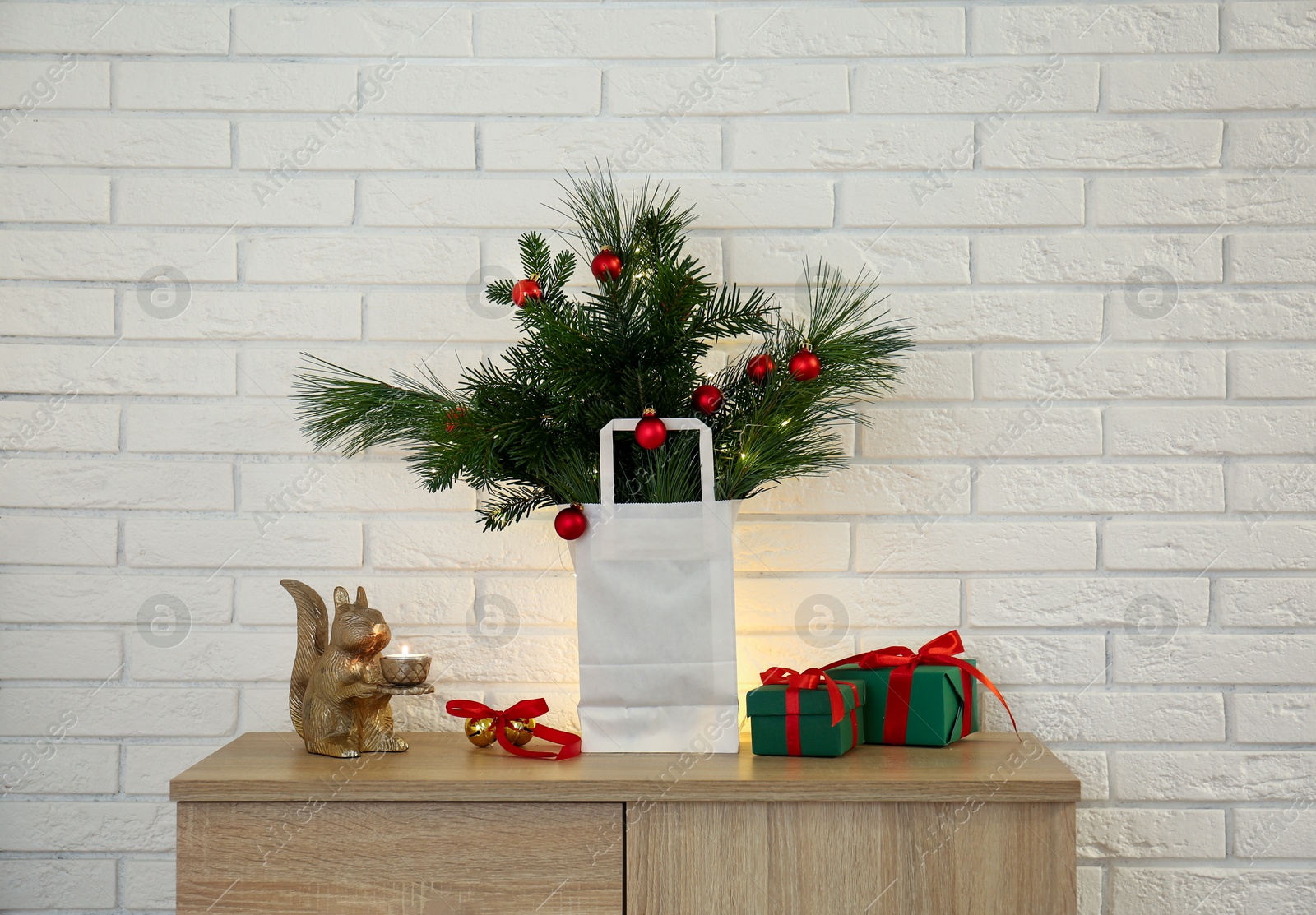 Photo of Beautiful Christmas composition of decorated fir and pine tree branches on wooden nightstand near white brick wall