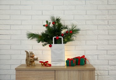 Photo of Beautiful Christmas composition of decorated fir and pine tree branches on wooden nightstand near white brick wall