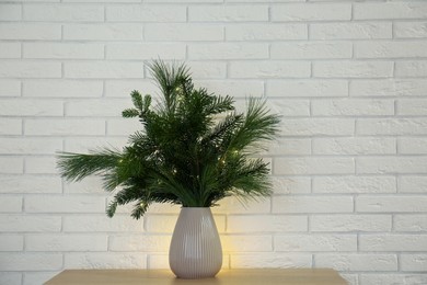 Photo of Beautiful Christmas composition of decorated fir and pine tree branches on wooden table near white brick wall