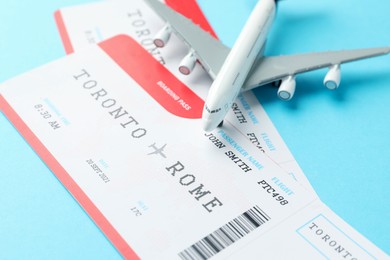 Photo of Travel agency. Flight tickets and plane model on light blue background, closeup