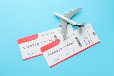 Photo of Travel agency. Flight tickets and plane model on light blue background, flat lay