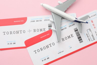 Photo of Travel agency. Flight tickets and plane model on pink background, flat lay