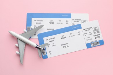 Photo of Travel agency. Flight tickets and plane model on pink background, flat lay