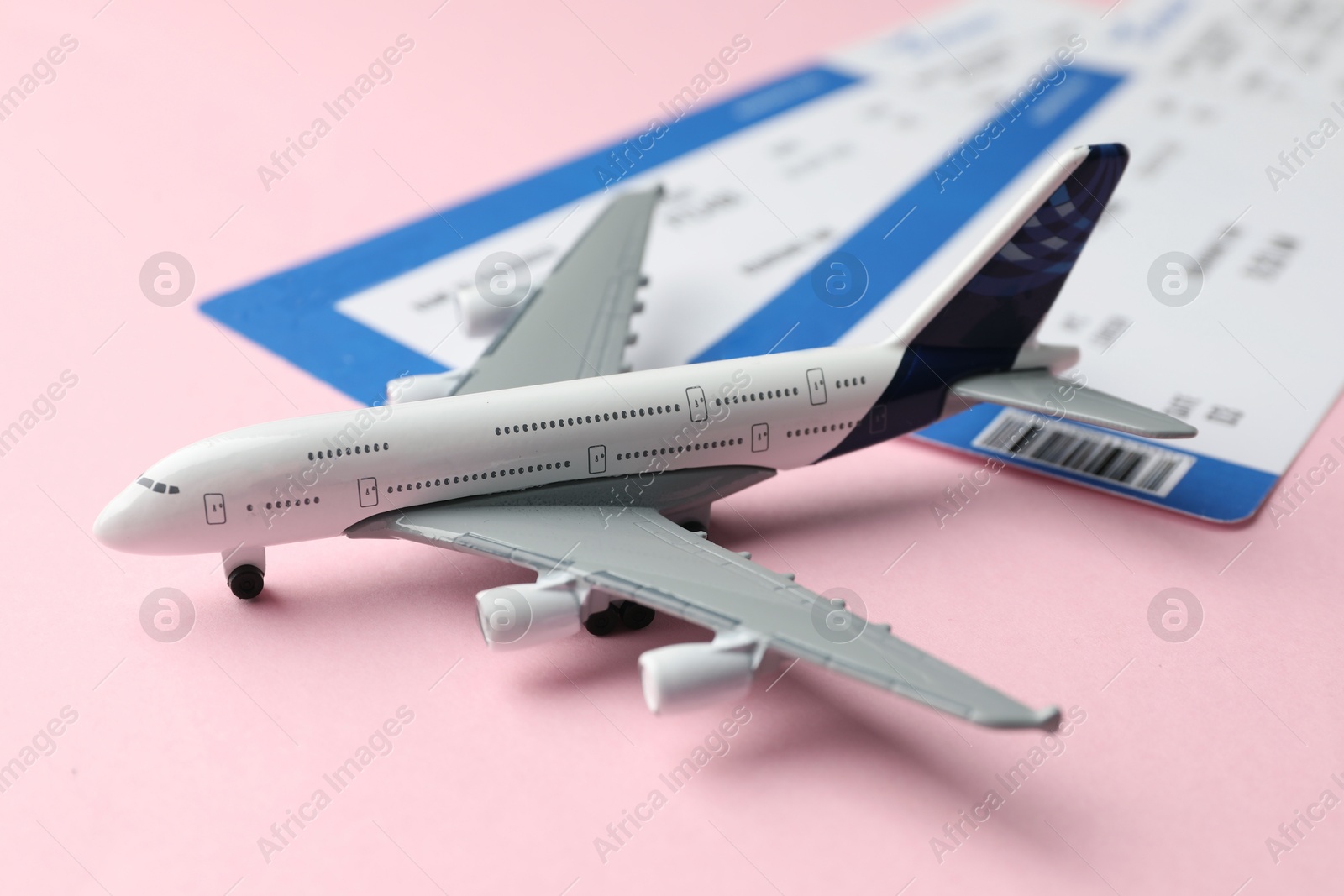 Photo of Travel agency. Flight tickets and plane model on pink background, closeup