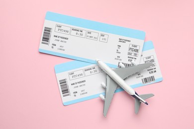 Photo of Travel agency. Flight tickets and plane model on pink background, flat lay