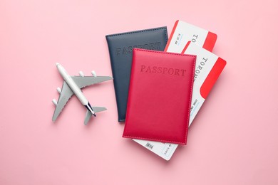 Photo of Travel agency. Flight tickets, passports and plane model on pink background, top view