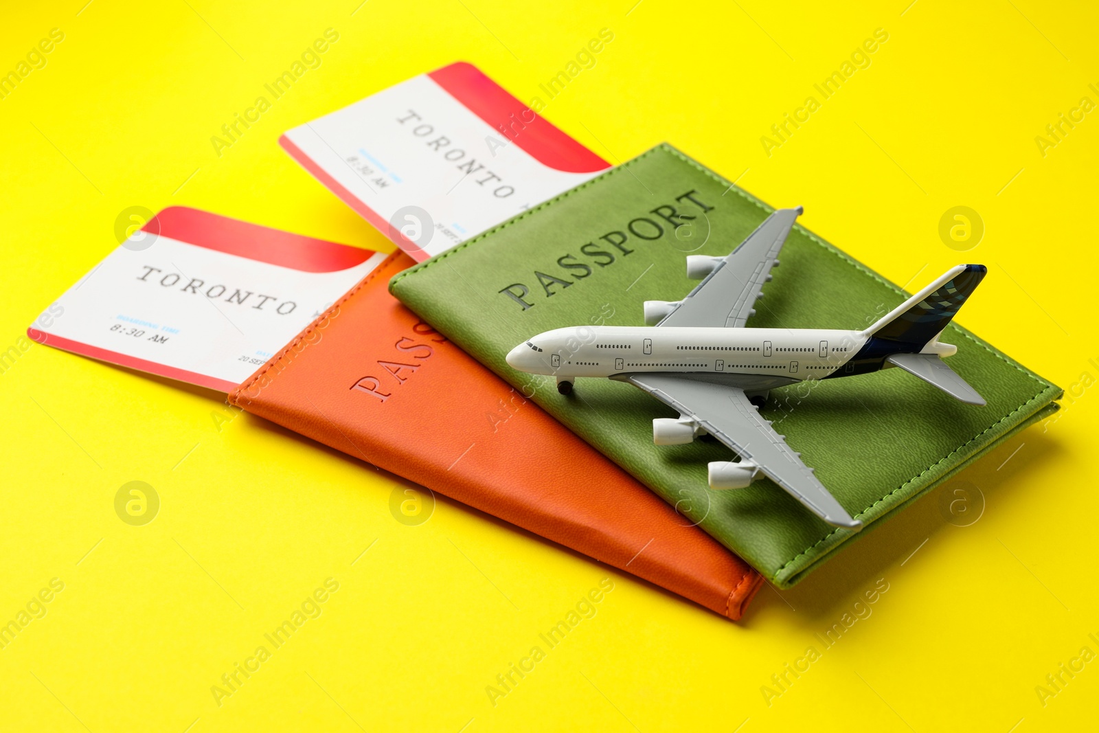 Photo of Travel agency. Flight tickets, passports and plane model on yellow background, closeup