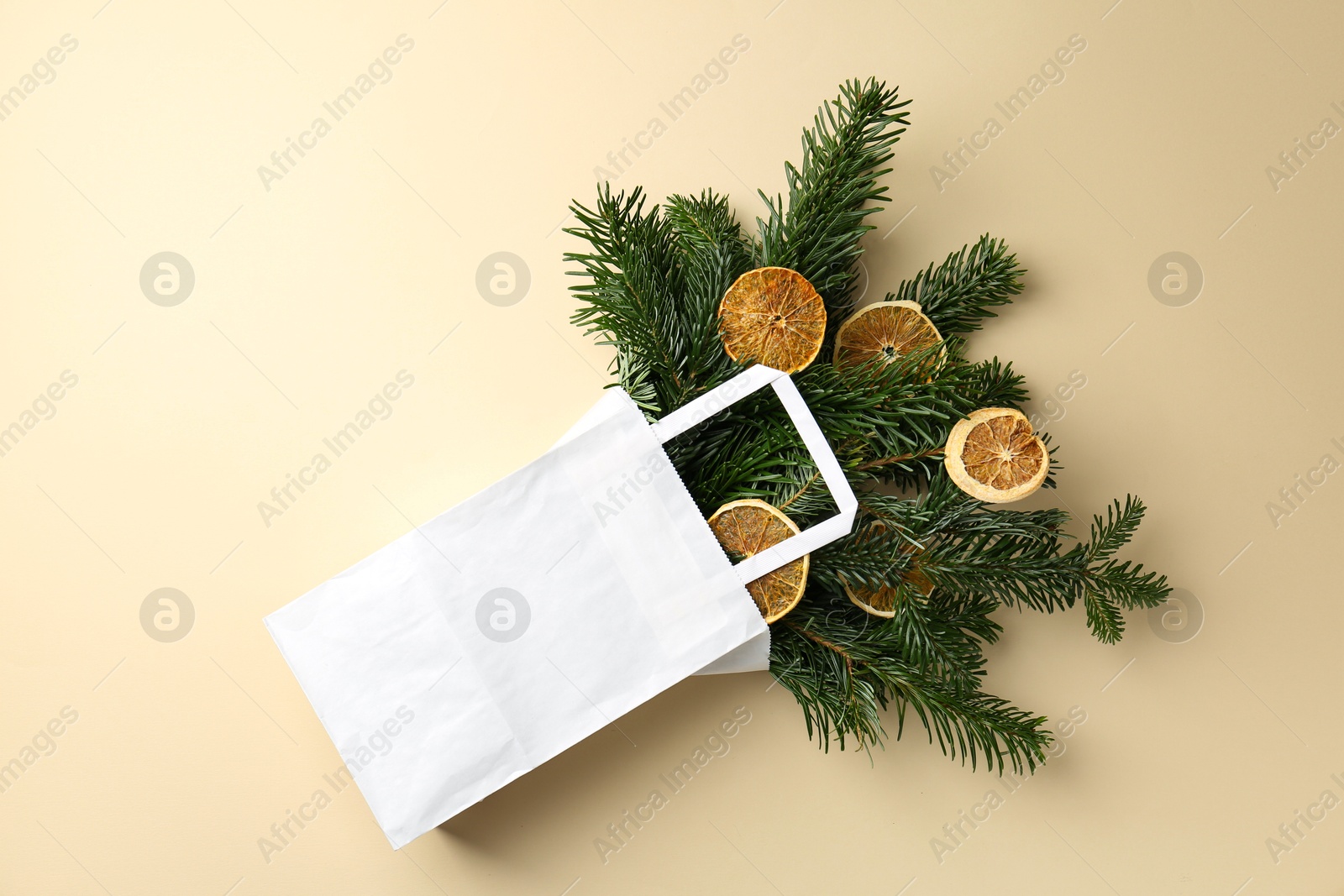 Photo of Christmas bouquet of fir tree branches with dry orange pieces in paper bag on beige background, top view