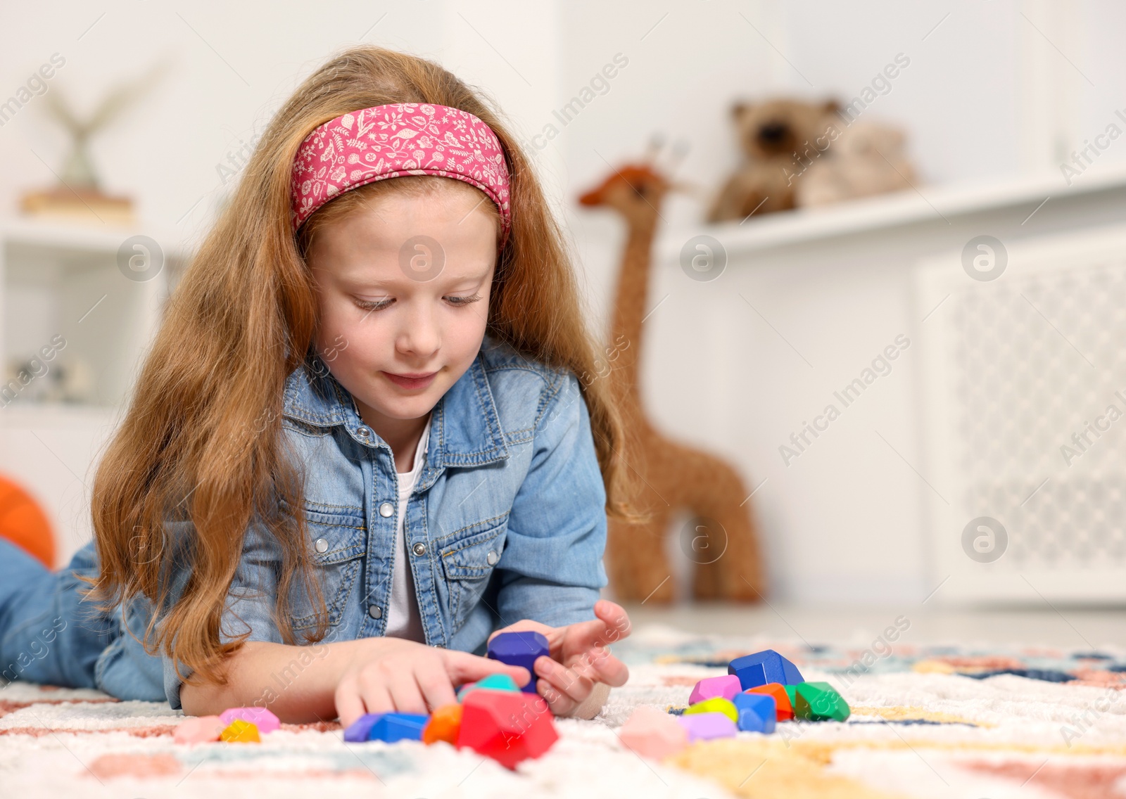 Photo of Little girl playing with balancing stones on floor indoors, space for text