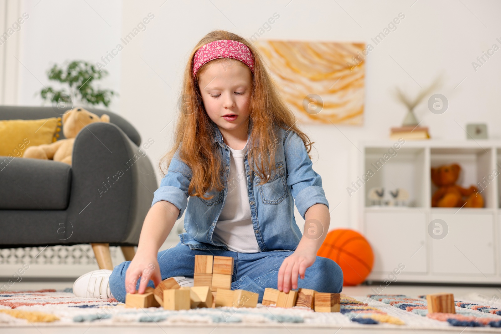 Photo of Little girl playing with wooden cubes on floor indoors