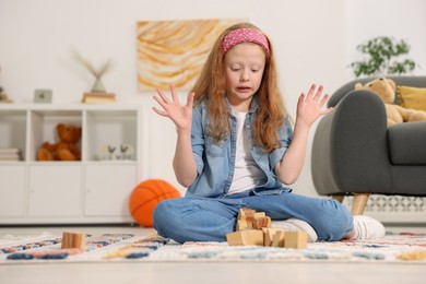 Photo of Little girl playing with wooden cubes on floor indoors, space for text