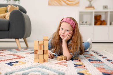 Photo of Little girl playing with wooden cubes on floor indoors